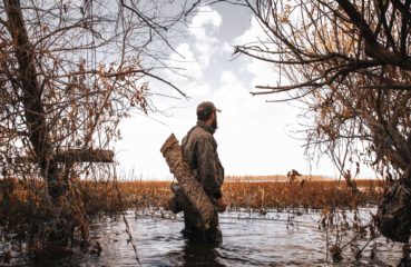 A duck hunter stands in a marsh