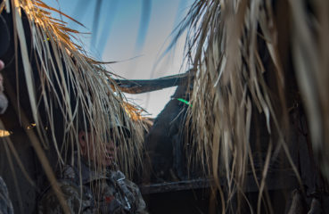 Duck hunters wait in a hunting blind with a black labrador retriever