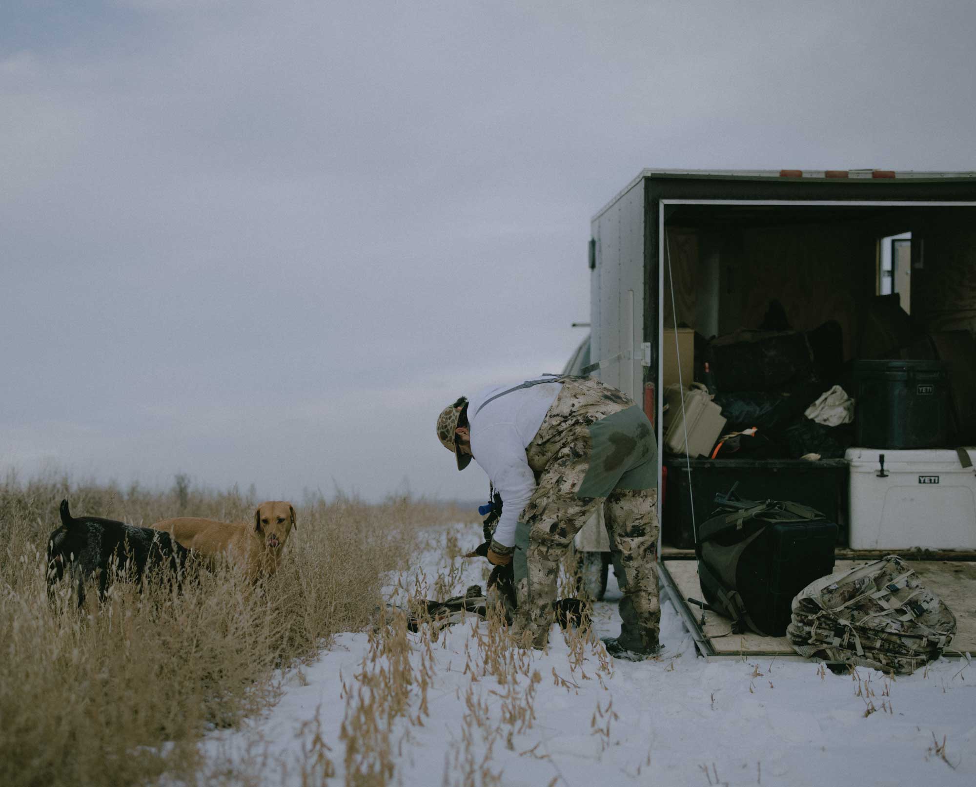 A truck bed with hunting gear and a yellow lab in a kennel