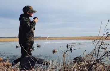 A young duck hunter looks out at a decoy spread in a pond