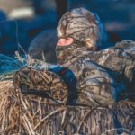 A young duck hunter dressed in camo waits in a layout blind