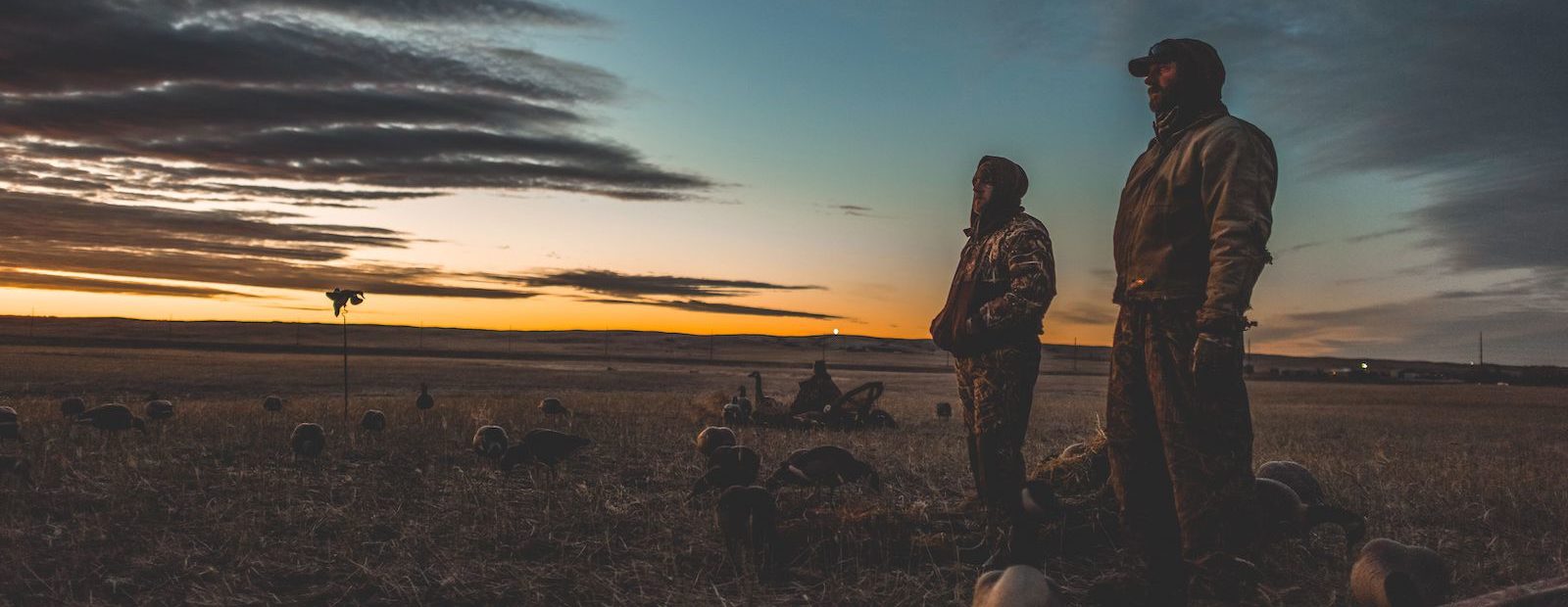 A pair of duck hunters looks across a field at sunrise