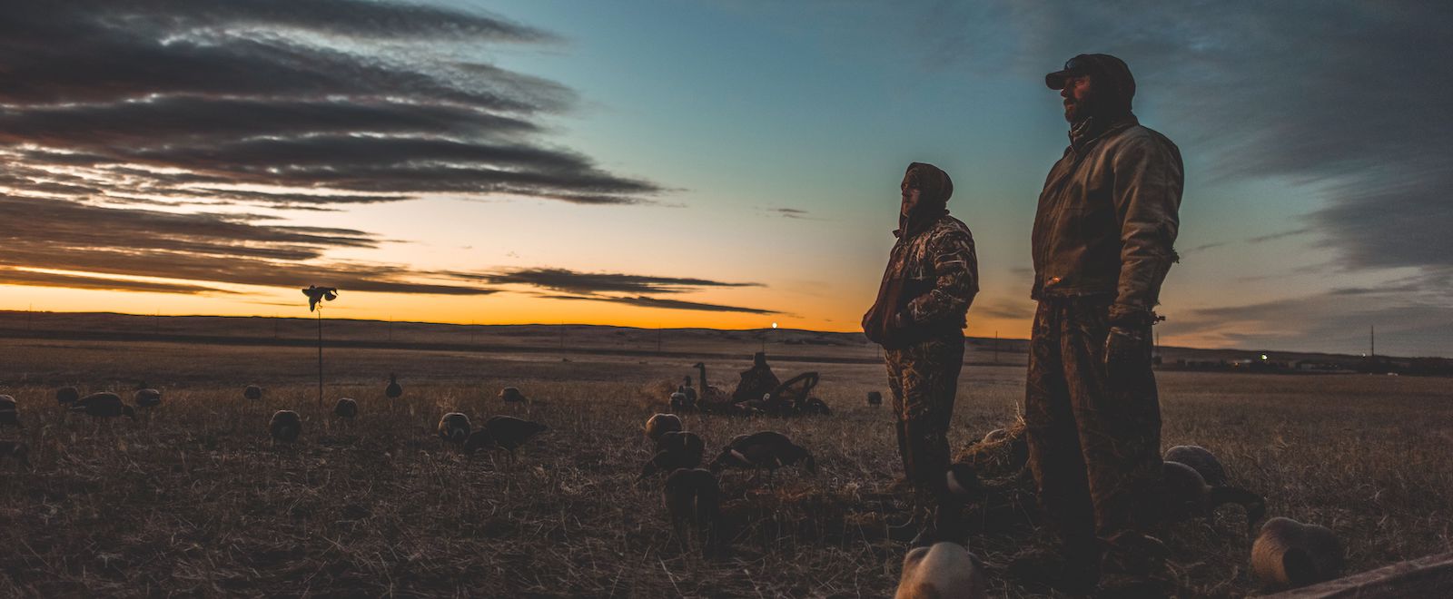 A pair of duck hunters looks across a field at sunrise