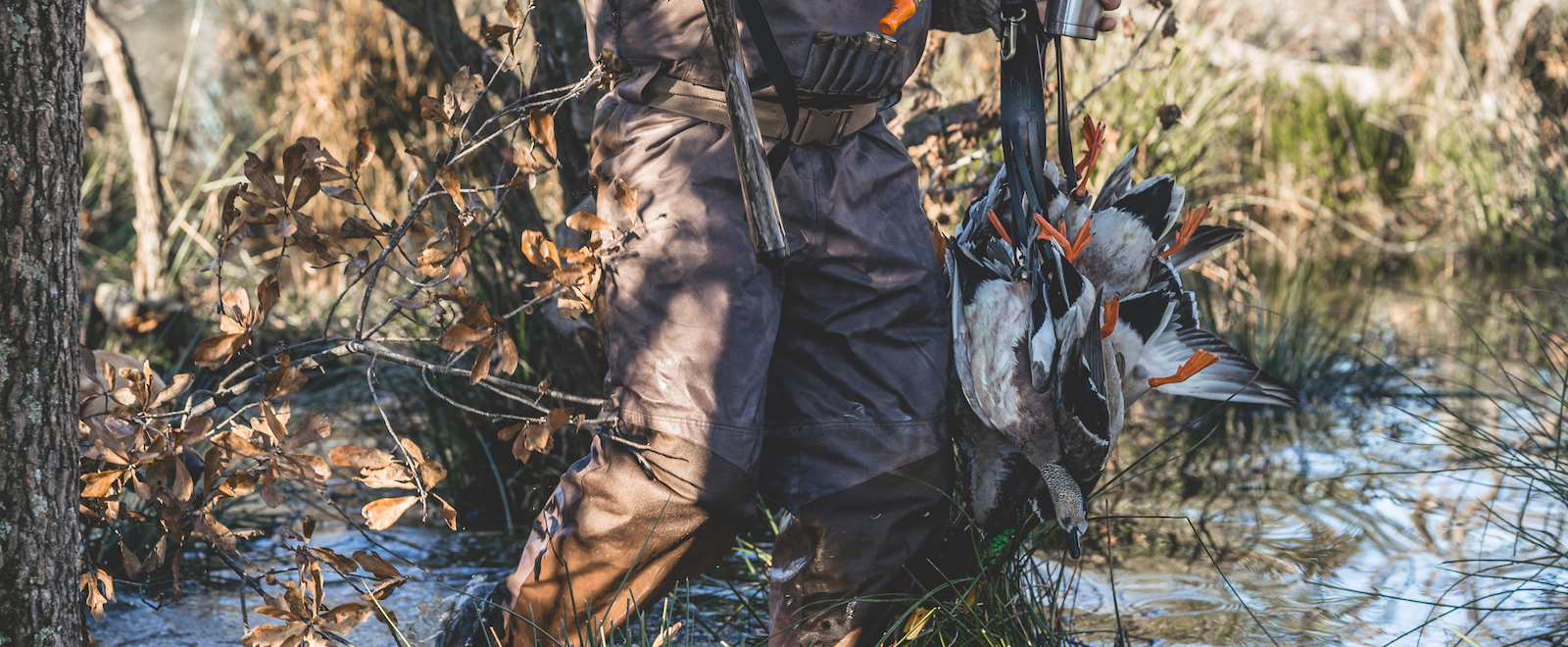 A duck hunter wearing breathable waders walks through flooded timber